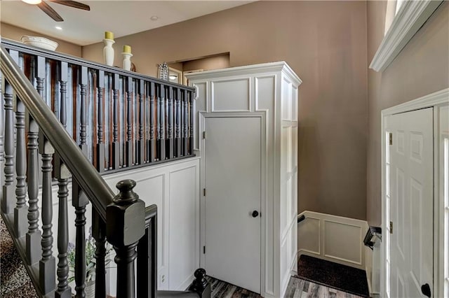 stairway featuring a wainscoted wall, ceiling fan, a decorative wall, and wood finished floors