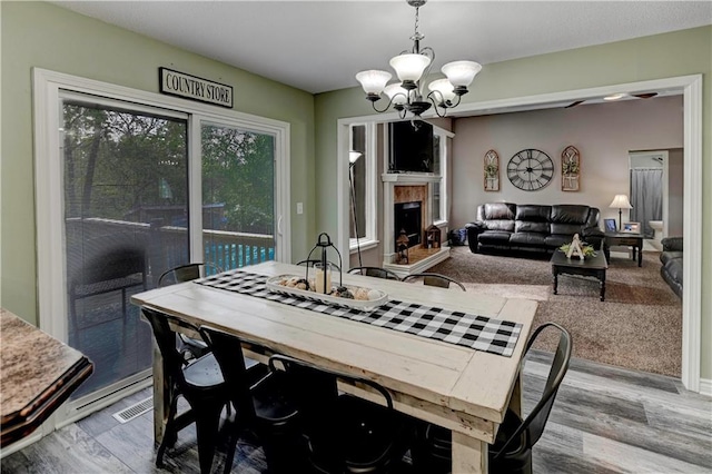 dining room featuring a fireplace with raised hearth, a notable chandelier, and wood finished floors