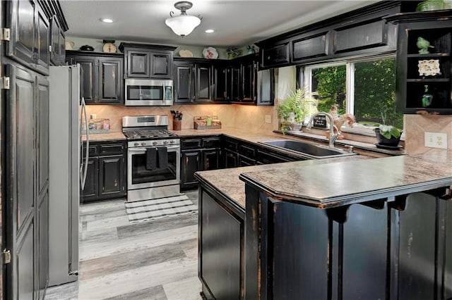 kitchen featuring a sink, dark cabinetry, stainless steel appliances, a peninsula, and tasteful backsplash