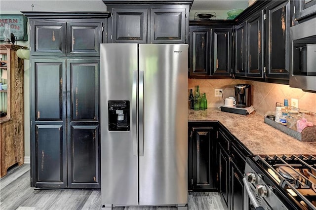 kitchen featuring light wood-style floors, decorative backsplash, light countertops, dark cabinets, and stainless steel appliances