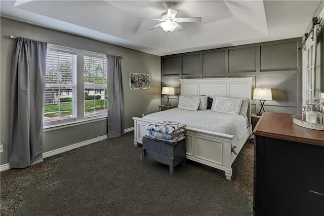 bedroom featuring a ceiling fan, baseboards, a tray ceiling, and dark colored carpet