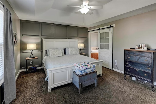 bedroom with dark carpet, a barn door, a ceiling fan, and a decorative wall