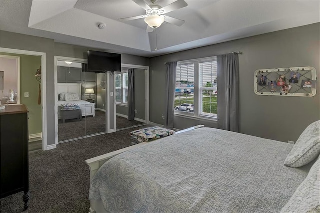 carpeted bedroom featuring baseboards, a raised ceiling, multiple closets, and ceiling fan