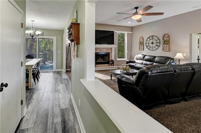 living area featuring baseboards, ceiling fan with notable chandelier, wood finished floors, and a tiled fireplace