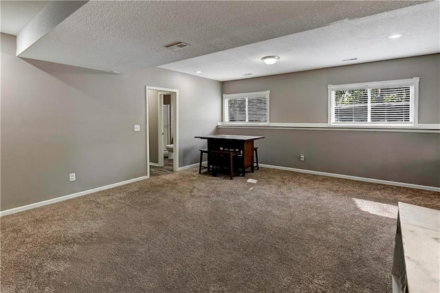 below grade area with carpet floors, a textured ceiling, baseboards, and visible vents