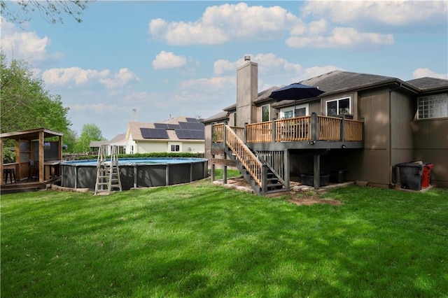 back of house featuring a chimney, a deck, an outdoor pool, a yard, and stairs