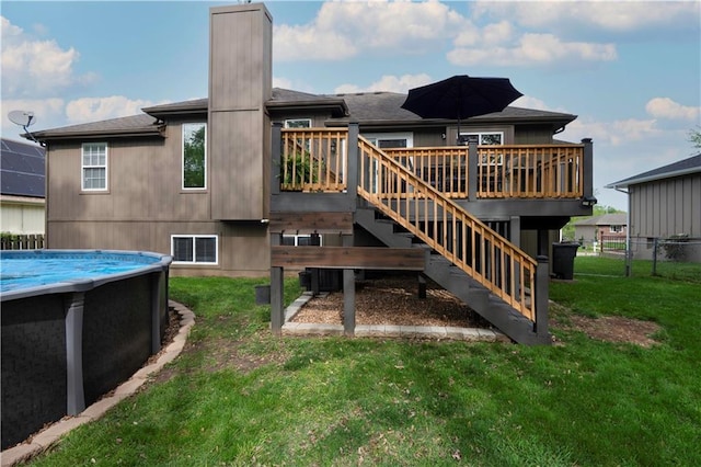 rear view of property with a deck, an outdoor pool, fence, a yard, and stairs