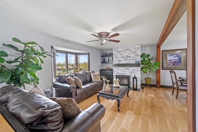 living area featuring a fireplace, light wood-type flooring, a ceiling fan, and baseboards