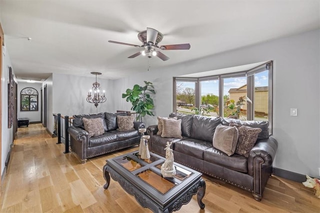 living room featuring light wood-style floors, baseboards, and ceiling fan with notable chandelier