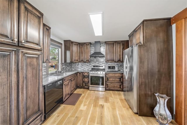 kitchen featuring wall chimney range hood, light wood-style flooring, a sink, stainless steel appliances, and backsplash