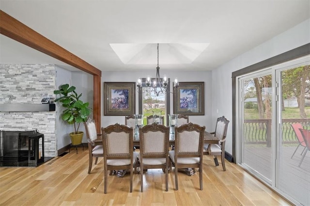 dining area with a skylight, a notable chandelier, light wood-style flooring, and a fireplace