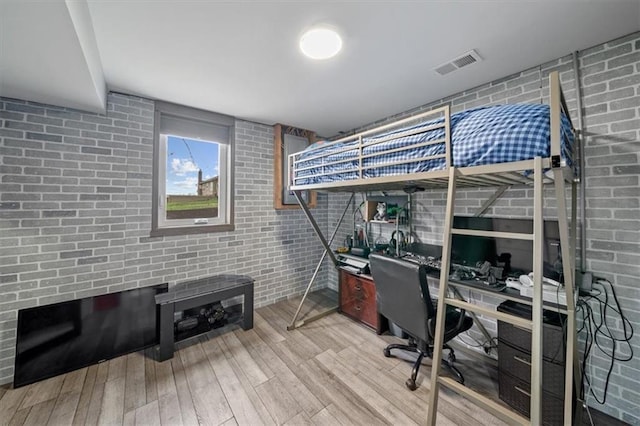 bedroom featuring visible vents, wood finished floors, and brick wall