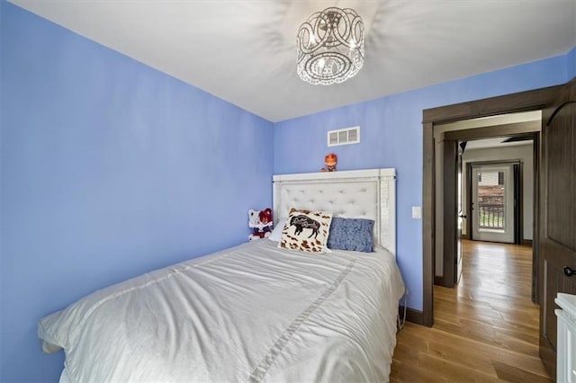 bedroom with a chandelier, visible vents, wood finished floors, and baseboards