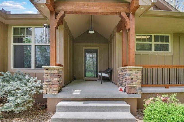 view of exterior entry featuring board and batten siding, covered porch, and stone siding