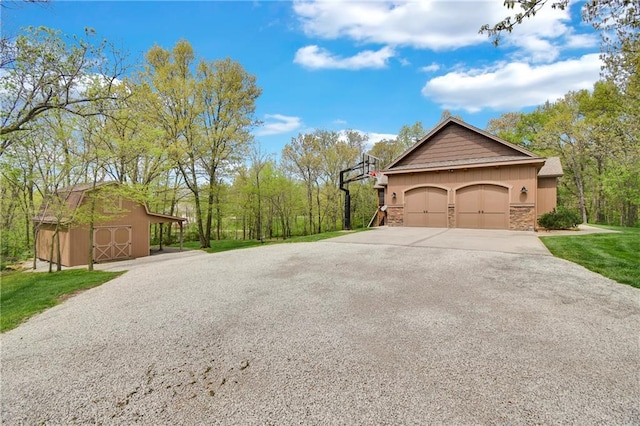 view of side of home featuring an attached garage, stone siding, concrete driveway, a barn, and an outbuilding