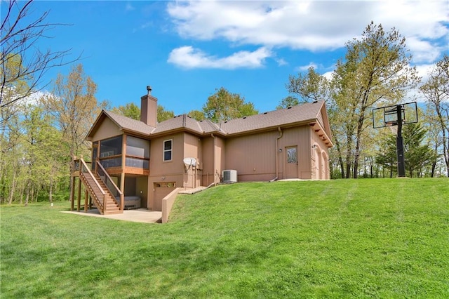 rear view of property featuring a sunroom, stairway, a chimney, central air condition unit, and a yard