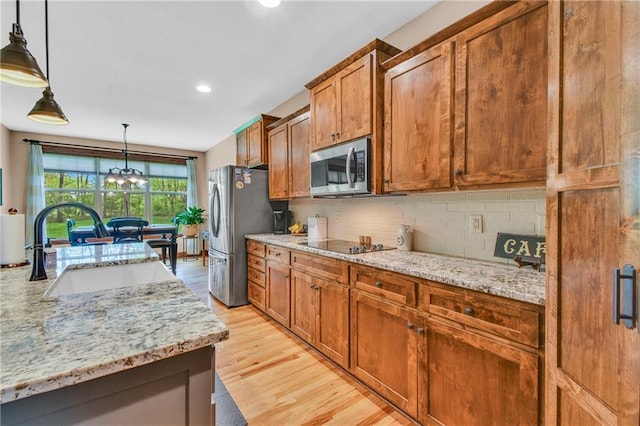 kitchen featuring appliances with stainless steel finishes, a sink, a chandelier, brown cabinetry, and backsplash