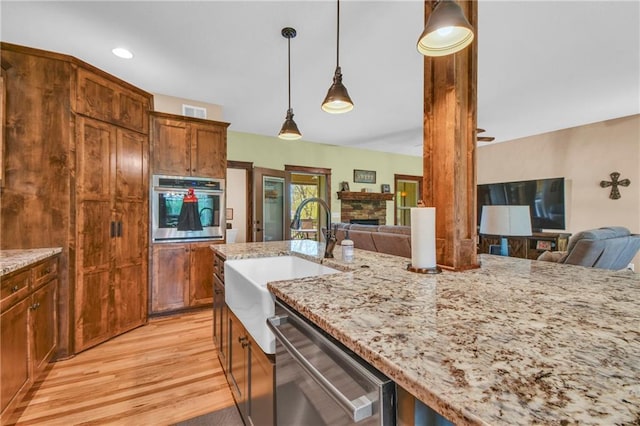 kitchen featuring appliances with stainless steel finishes, light stone countertops, light wood-type flooring, a sink, and open floor plan