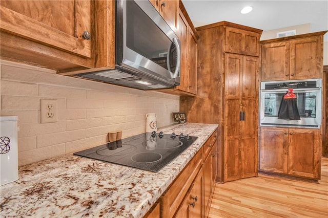 kitchen featuring backsplash, appliances with stainless steel finishes, light stone countertops, light wood-type flooring, and brown cabinets