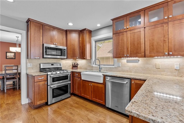 3610 NE Basswood Dr, Lees Summit, MO 64064 - kitchen featuring appliances with stainless steel finishes, a sink, light wood-type flooring, light stone counters, and brown cabinets