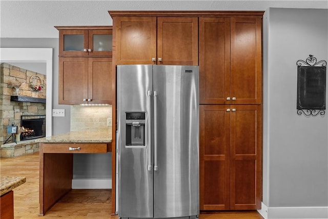 3610 NE Basswood Dr, Lees Summit, MO 64064 - kitchen featuring stainless steel fridge, light wood-style floors, light stone counters, glass insert cabinets, and a stone fireplace