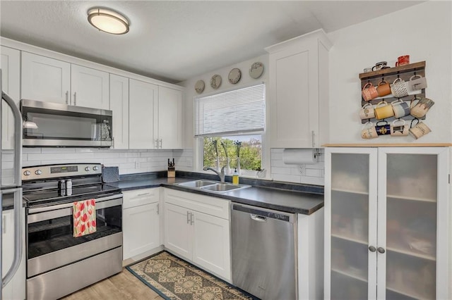 kitchen with white cabinets, dark countertops, a sink, stainless steel appliances, and decorative backsplash