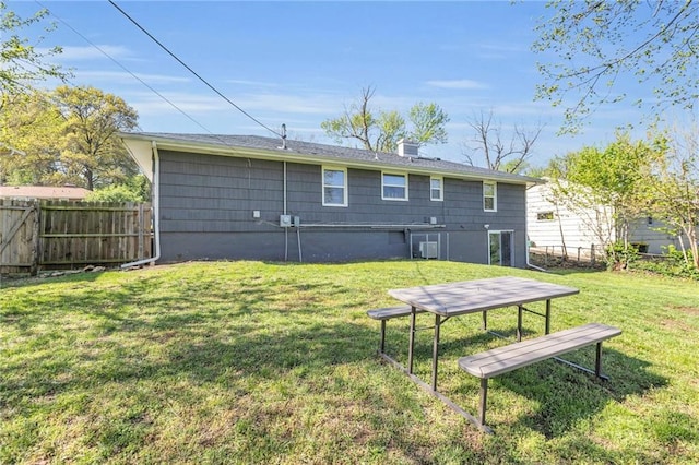 back of house featuring central air condition unit, fence, a yard, and a chimney