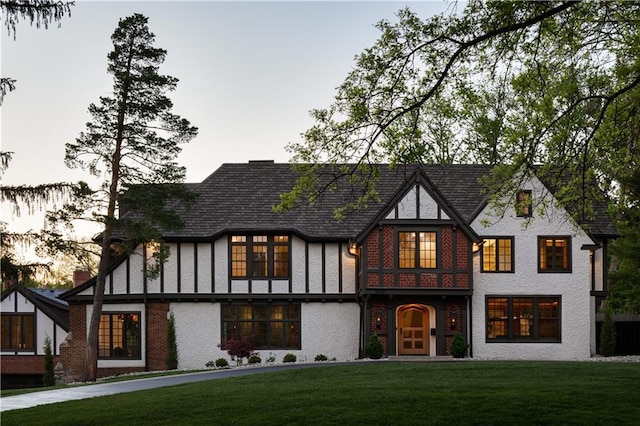 tudor-style house featuring brick siding and a front yard