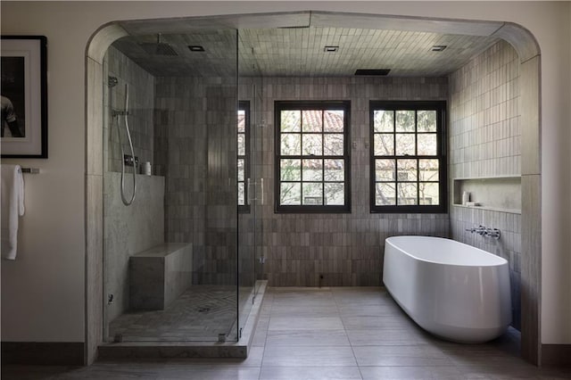 full bathroom with tile walls, tile patterned floors, a freestanding tub, and a shower stall