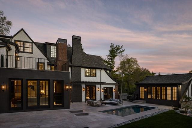 back of property at dusk featuring a chimney, an outdoor pool, a patio, and a balcony