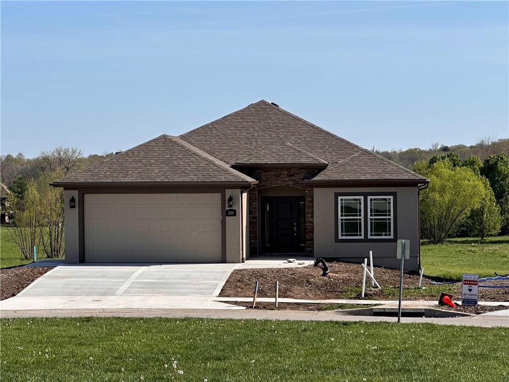 ranch-style home featuring concrete driveway, roof with shingles, a front yard, an attached garage, and stucco siding