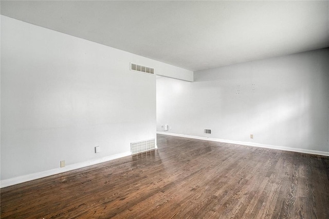unfurnished room featuring dark wood-style floors, visible vents, and baseboards