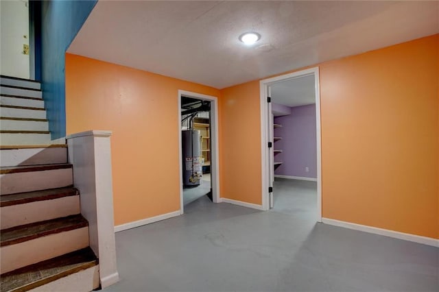 interior space with gas water heater, finished concrete flooring, stairway, and baseboards