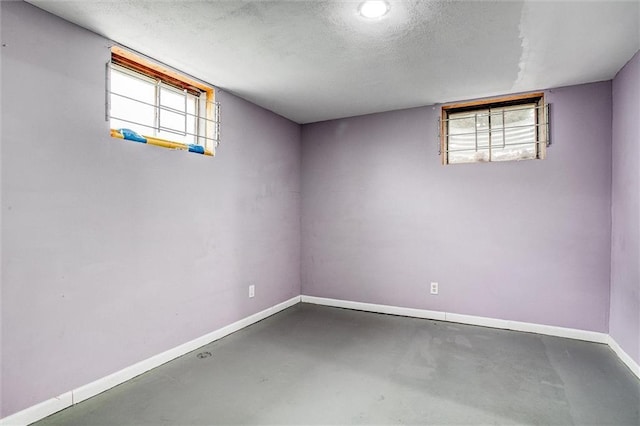 below grade area with baseboards, a textured ceiling, and plenty of natural light