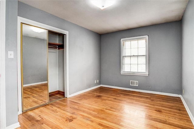 unfurnished bedroom with wood finished floors, visible vents, baseboards, and a closet