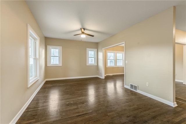 spare room featuring baseboards, visible vents, ceiling fan, and dark wood-style flooring