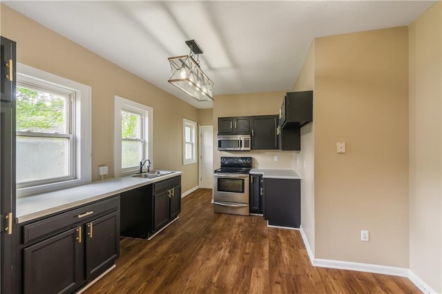 kitchen featuring appliances with stainless steel finishes, light countertops, a sink, baseboards, and dark wood-type flooring