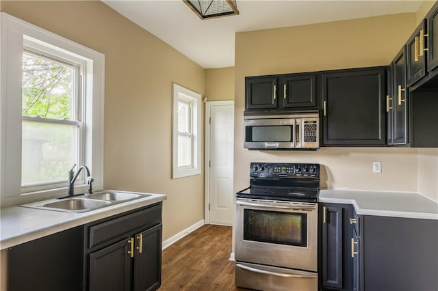 kitchen with dark wood-style floors, a sink, stainless steel appliances, light countertops, and baseboards
