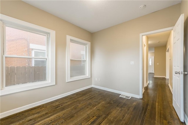 empty room with baseboards, visible vents, a wealth of natural light, and dark wood-type flooring