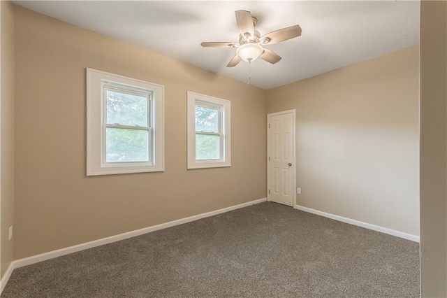 spare room featuring a ceiling fan, dark colored carpet, and baseboards