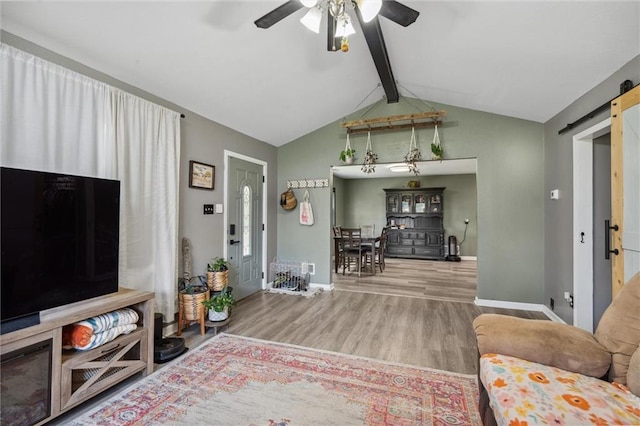 living room featuring a barn door, wood finished floors, vaulted ceiling with beams, ceiling fan, and baseboards