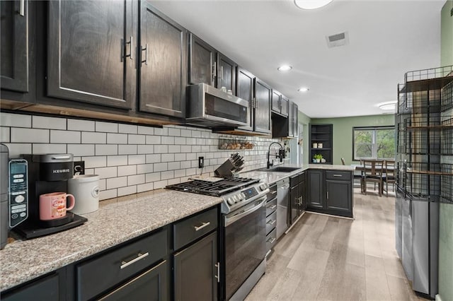 kitchen featuring a sink, decorative backsplash, light wood-style flooring, appliances with stainless steel finishes, and visible vents