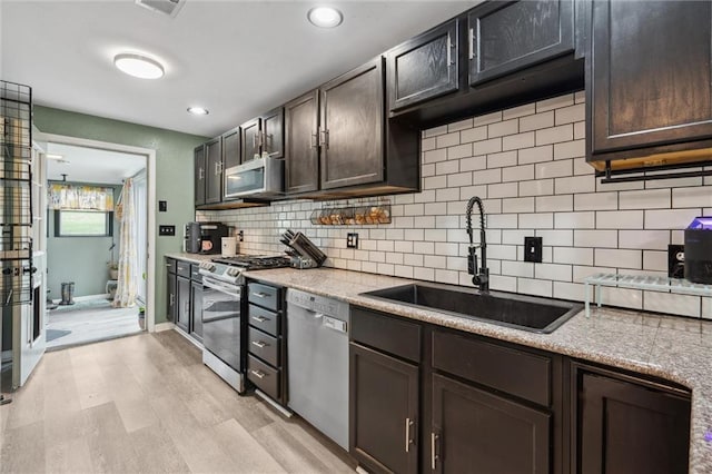 kitchen featuring stainless steel appliances, backsplash, dark brown cabinets, a sink, and light wood-style flooring