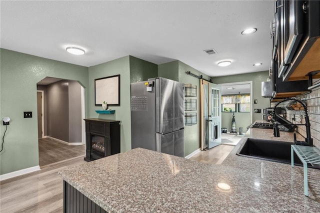 kitchen featuring light wood finished floors, baseboards, freestanding refrigerator, and arched walkways