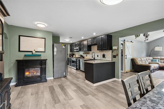 kitchen featuring stainless steel appliances, a sink, light wood-style floors, and a barn door