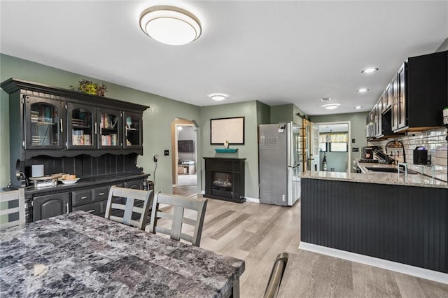 kitchen featuring light stone counters, light wood-style floors, arched walkways, a peninsula, and appliances with stainless steel finishes