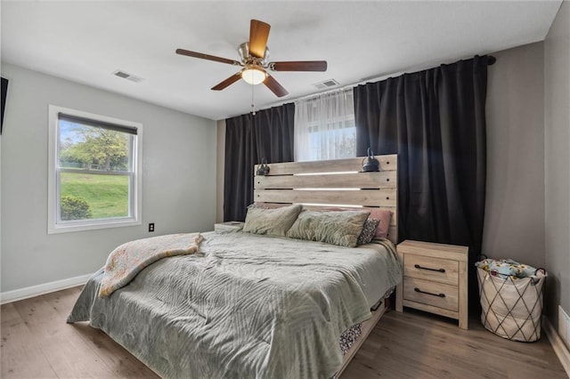 bedroom featuring baseboards, a ceiling fan, wood finished floors, and visible vents