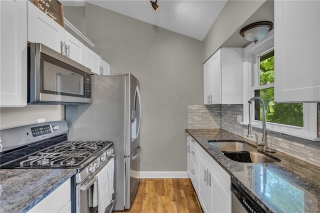 kitchen featuring decorative backsplash, a sink, baseboards, dark stone countertops, and stainless steel appliances