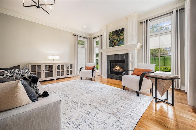 living room with crown molding, a tiled fireplace, wood finished floors, and a chandelier