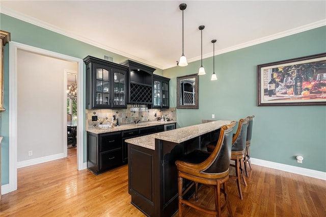 bar with backsplash, wet bar, light wood-type flooring, baseboards, and ornamental molding